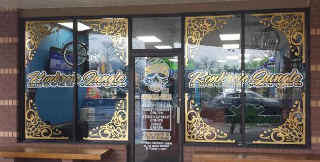 Konkrete Jungle Kustom Tattoo storefront with gold scrollwork and shop name on the windows; skull logo and shop hours on the glass door
