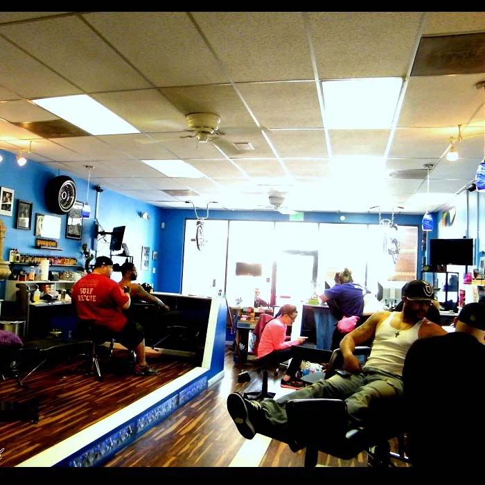 Busy shop interior with artists working at stations under a drop ceiling with ceiling fans, front windows in the back